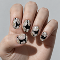 A close-up of a hand with manicured nails featuring a modern abstract design of black, white, and metallic gold marbled patterns.
