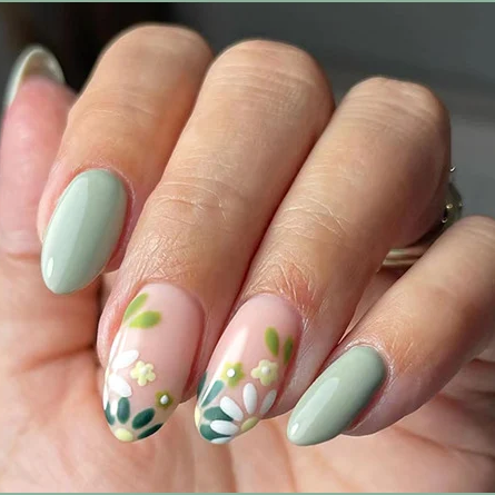 A close-up of a hand showcasing manicured press-on nails. The nails feature a mix of solid sage green and pale pink bases with delicate hand-painted floral designs in white, green, and yellow.